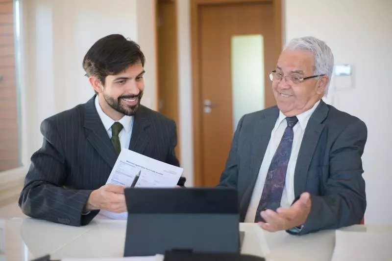Deux hommes souriants regardant une tablette dans un bureau.
