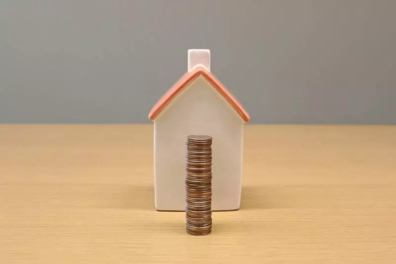 Un petit modèle de maison avec quelques pièces de monnaie devant.